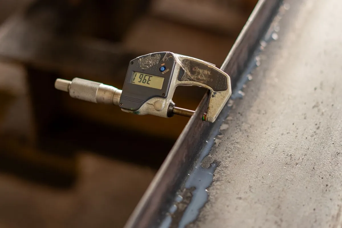 Stock photograph of a digital micrometer measuring a metal edge; not Omita inspection equipment.